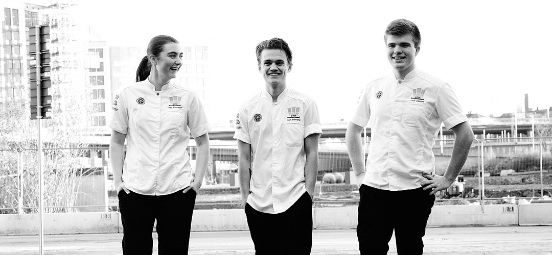 Svartvit bild av Tilda Svensson, Carl Böhrens och Love Lidström när de går ute på trottoaren med händerna i fickorna. De är glada och skrattar.